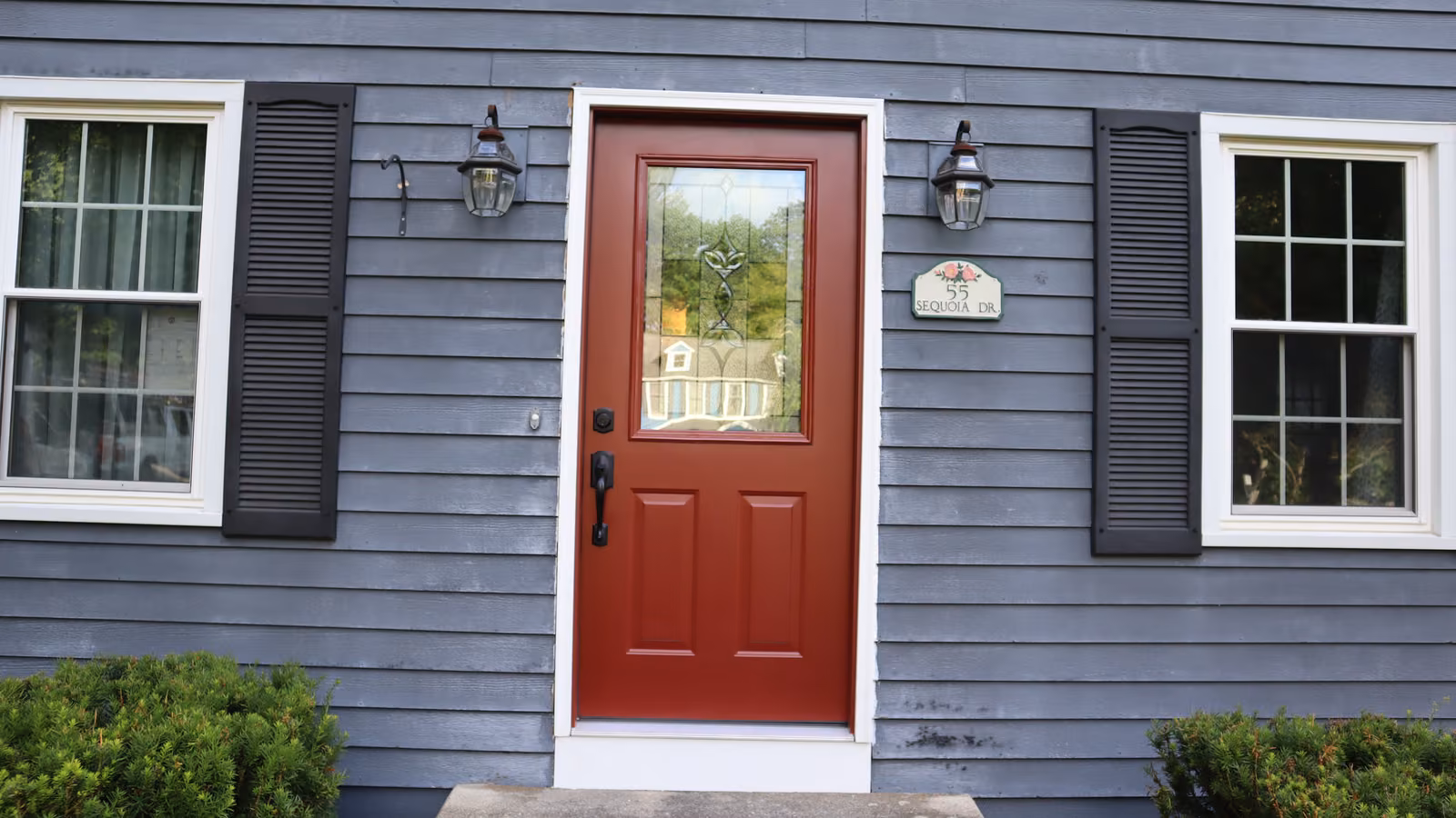 Red entry door with a decorative glass insert on a gray vinyl siding home