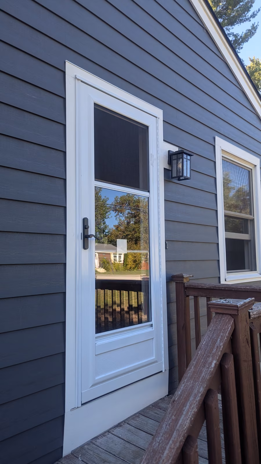 White storm door with a half-screen panel installed on gray vinyl siding