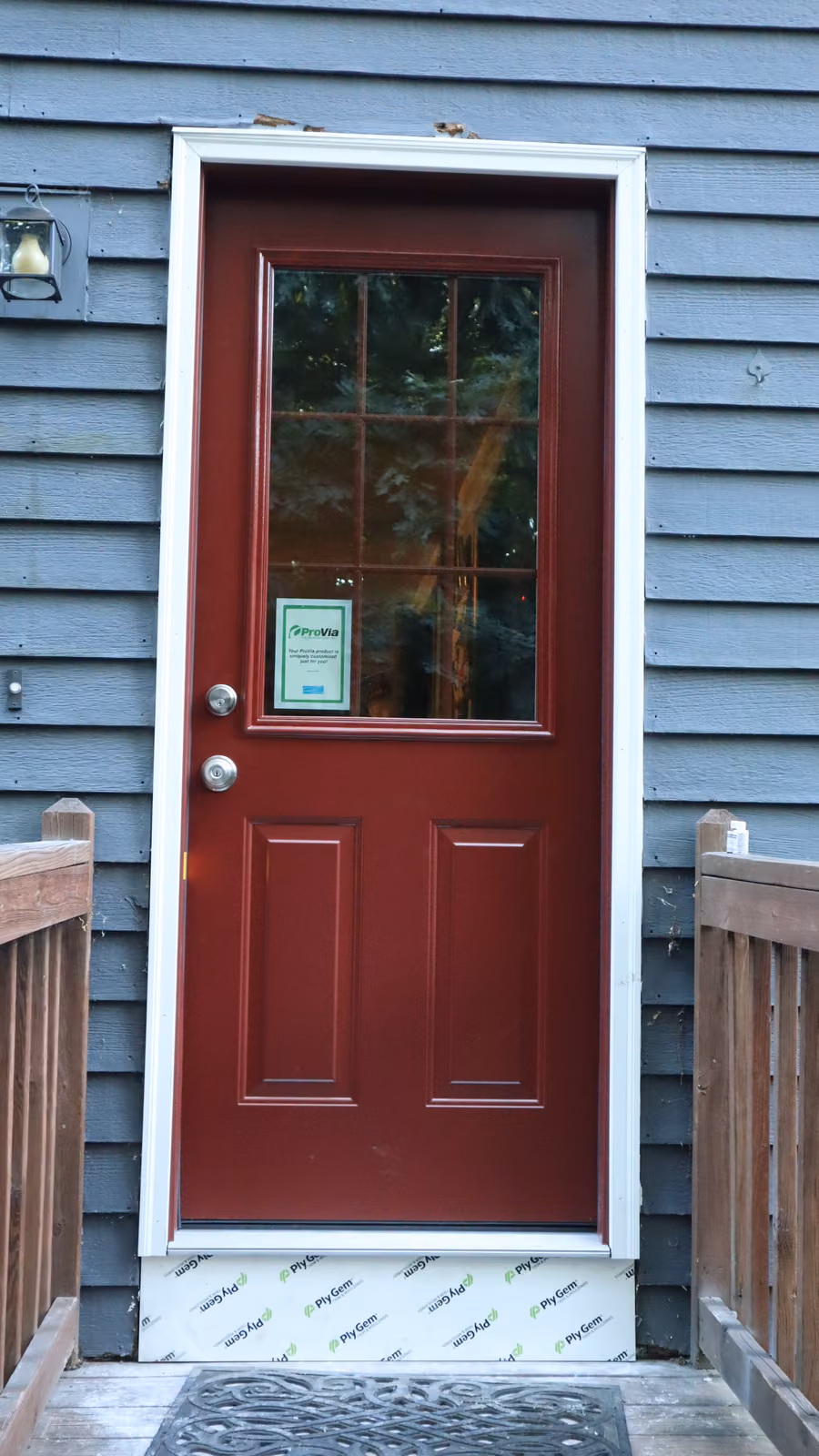 Red 9-lite steel entry door with brushed nickel hardware on gray clapboard siding