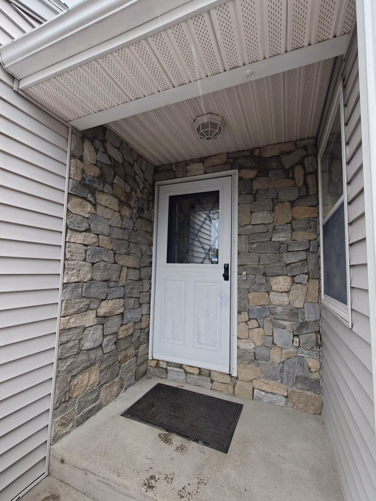 Covered entryway clad in mixed stone veneer with a white storm door and concrete landing