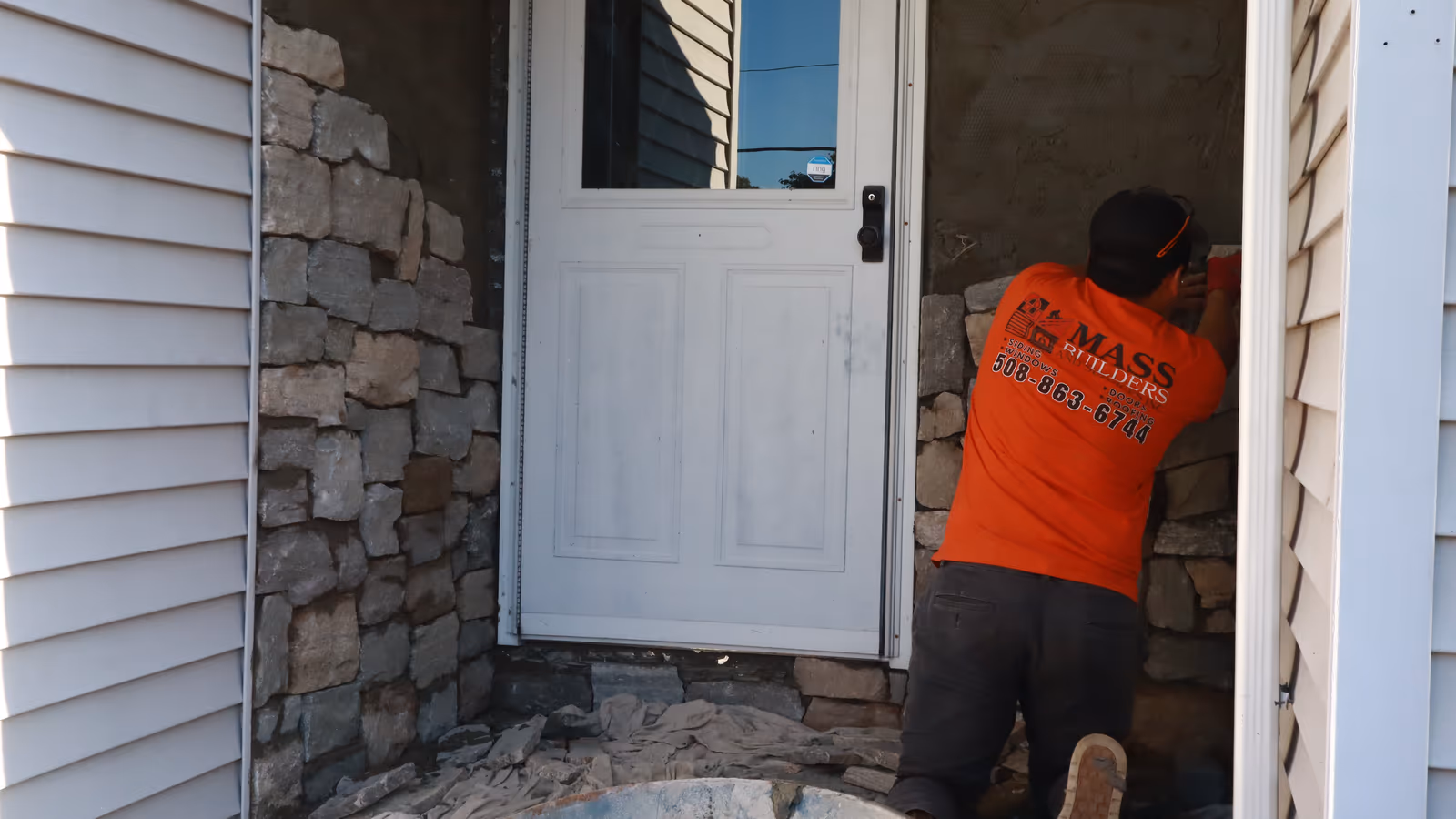 Installer fitting stone veneer at a white-door entrance during a hardscape project