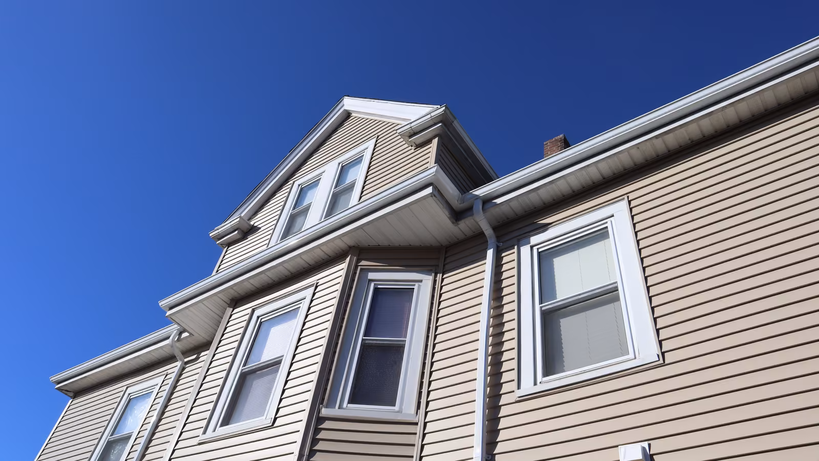 Close-up of a new vinyl siding gable with aluminum gutters and white corner trim
