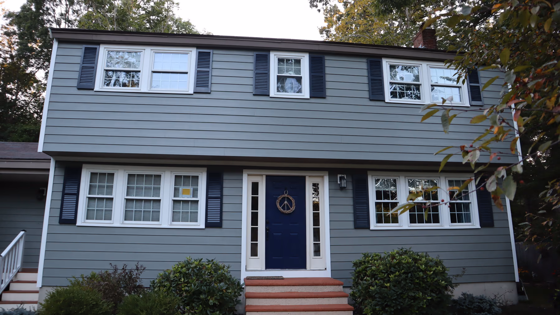 Colonial home in Holliston, MA with new sage-green vinyl lap siding, black shutters and white trim across the front elevation