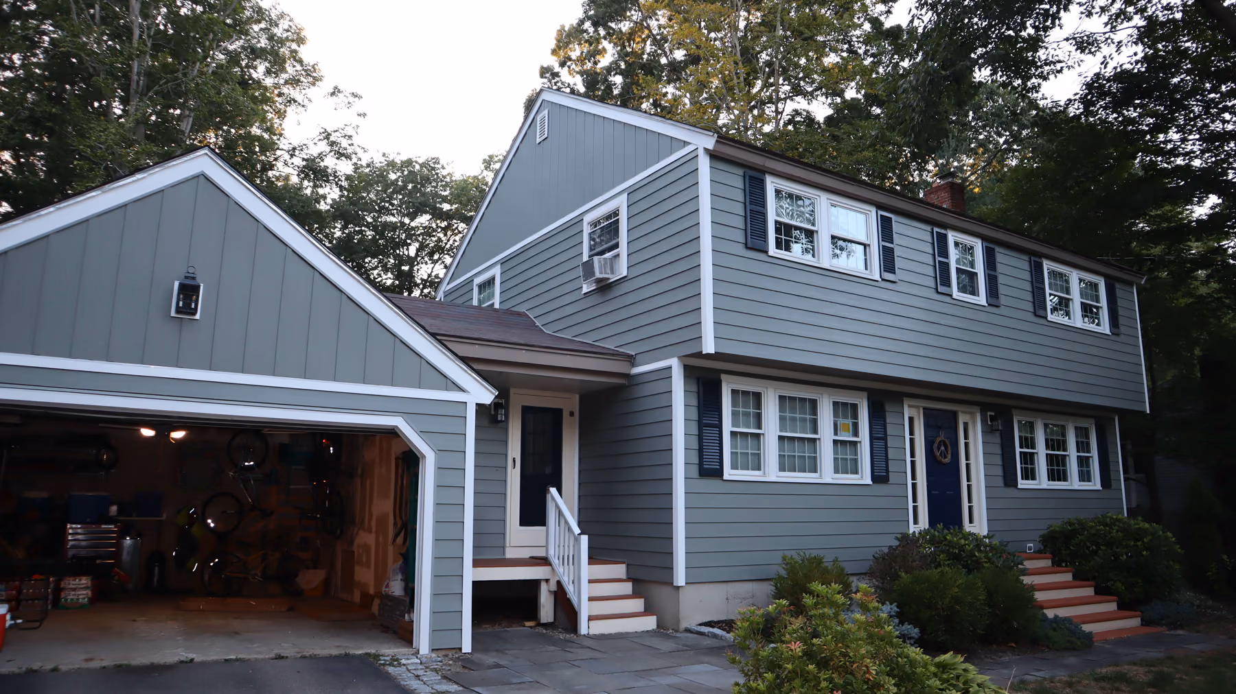 Front-quarter view of a Holliston colonial with new green vinyl siding, attached garage and stone chimney