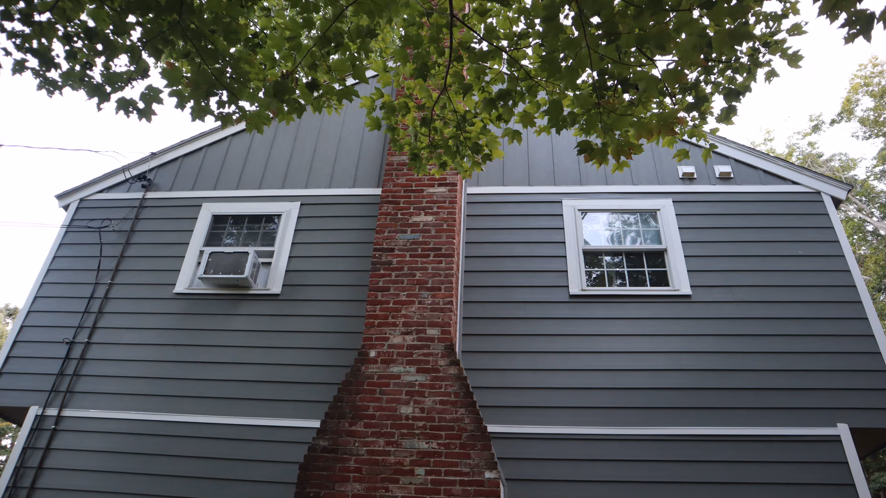 Side elevation of the home with new green vinyl siding around an original brick chimney