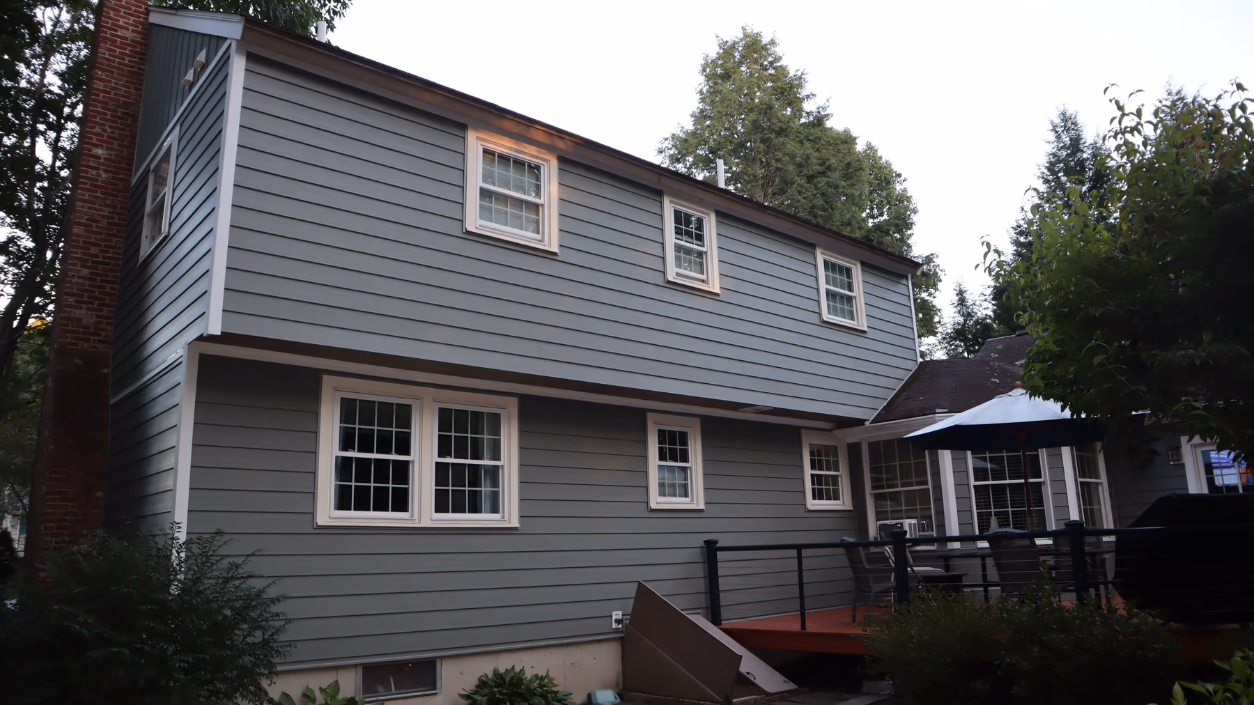 Rear elevation of the Holliston home with new green siding, gable dormer and a raised deck