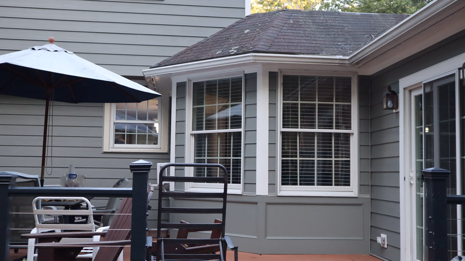 Bay window on the rear sunroom clad in new green vinyl siding with white trim, viewed from the deck