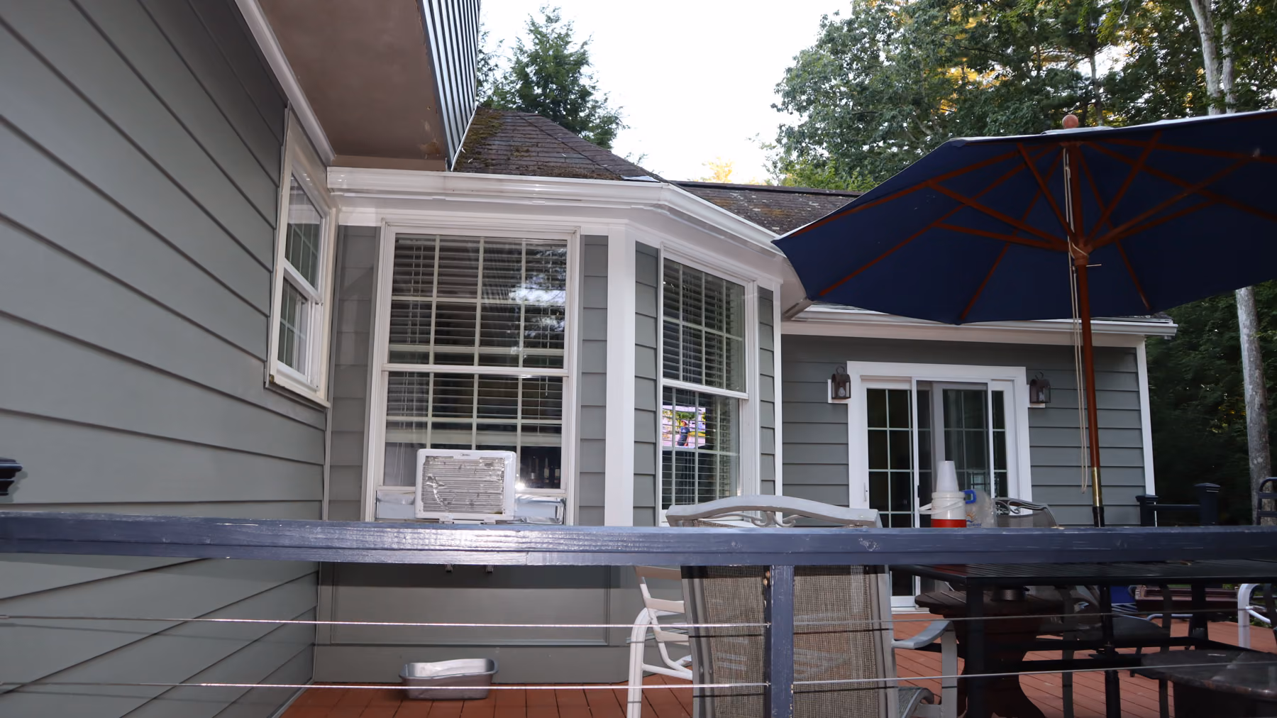 Side view of the sunroom bay with new green siding, from the deck under a shade umbrella