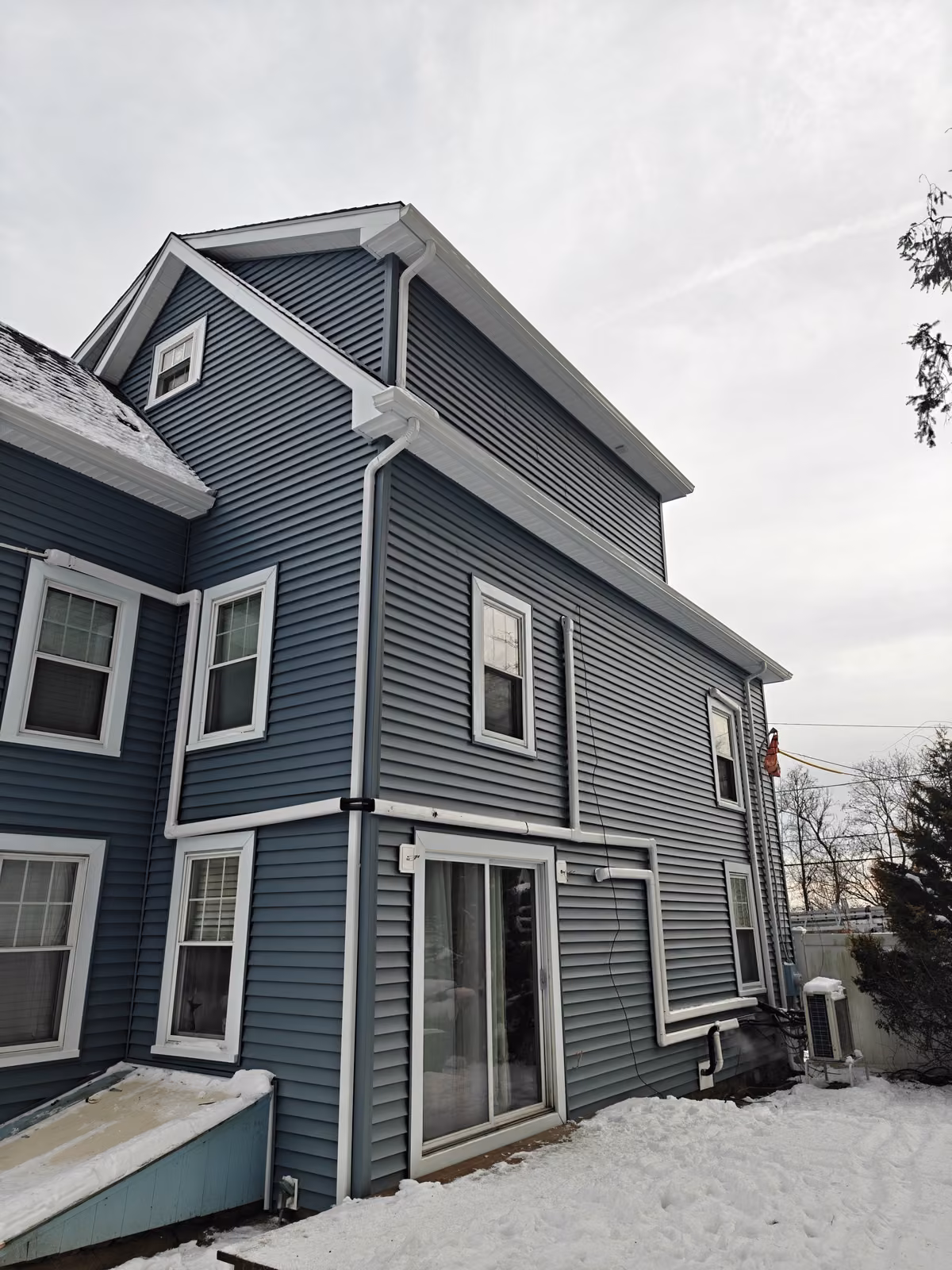 Rear corner of a colonial home with new dark blue vinyl siding and updated gutters