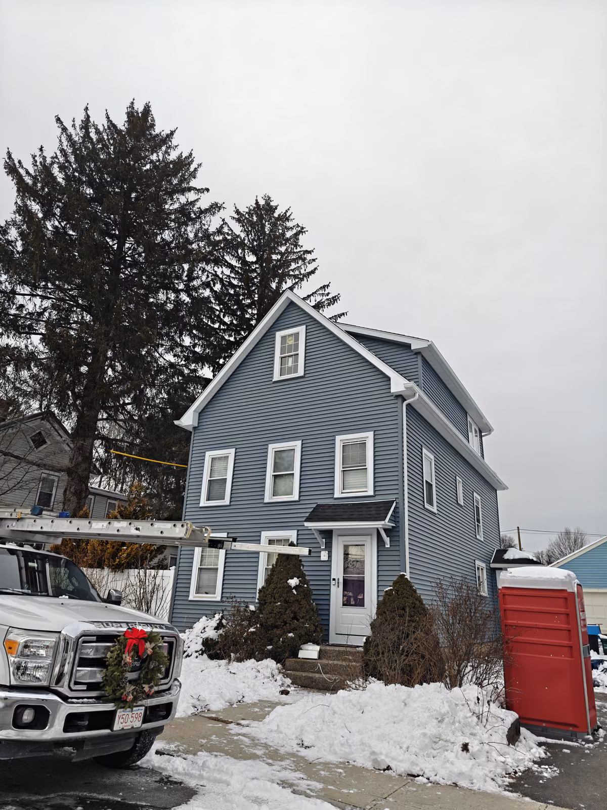 Front elevation of a three-story colonial after dark blue vinyl siding replacement