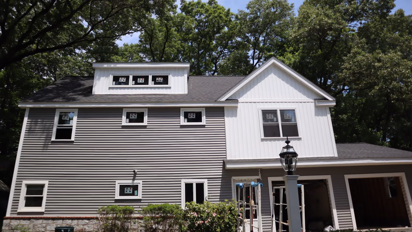 Gray horizontal vinyl siding with white board-and-batten gable on a two-story colonial
