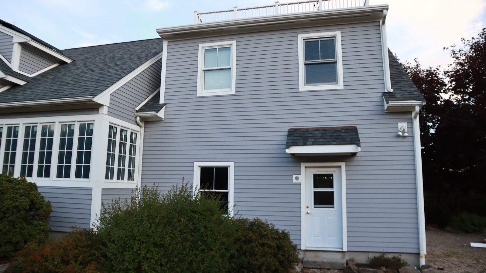 Coastal three-quarter view of a home with new lap siding, a bay window and white trim in golden-hour light