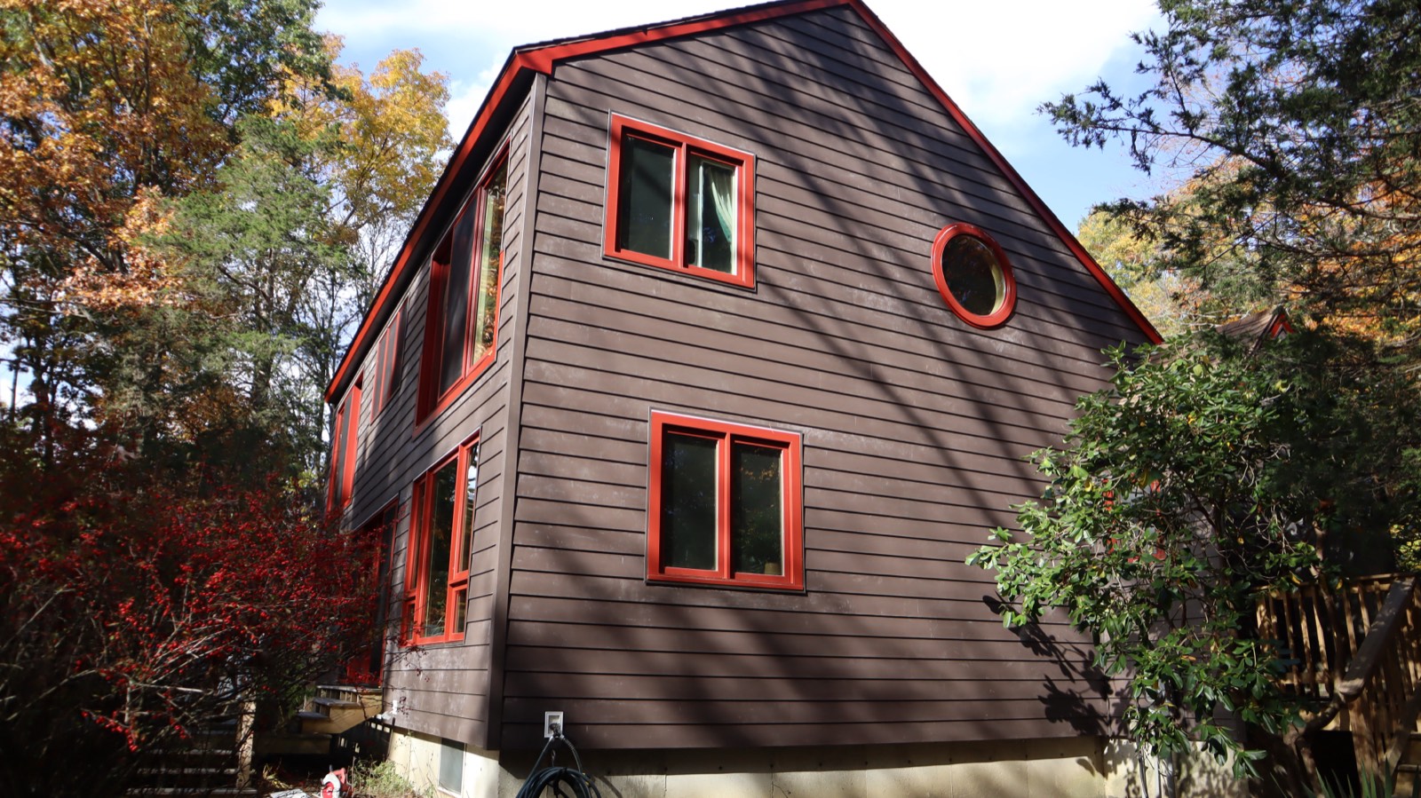 Dark brown lap siding with red trim and a round accent window under a clear blue sky