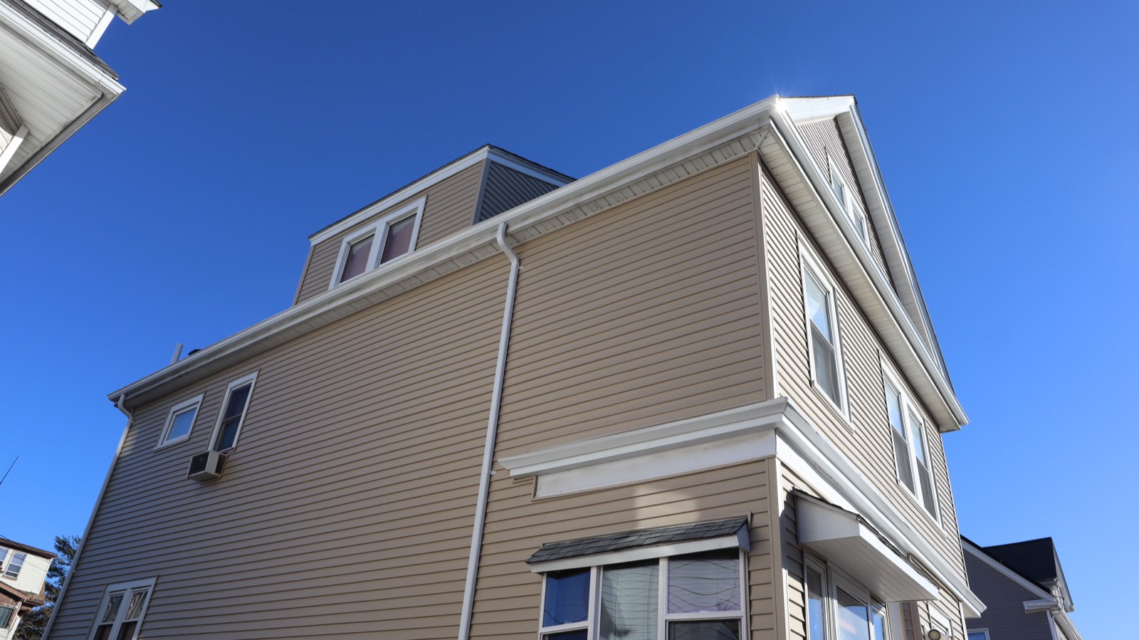 Corner of a tan three-decker with new vinyl siding against a deep blue sky