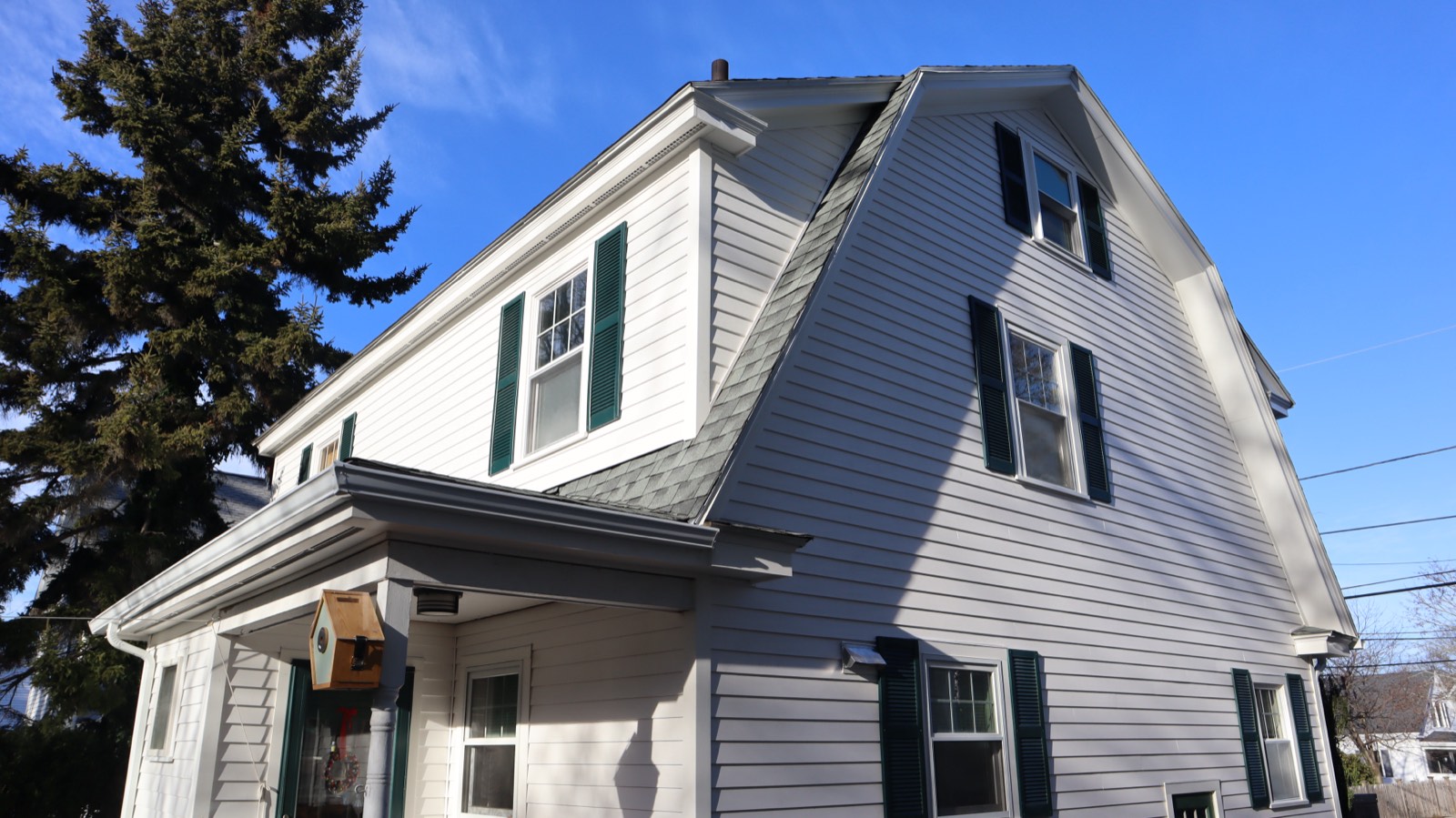White gambrel home with green shutters and new siding under a blue sky