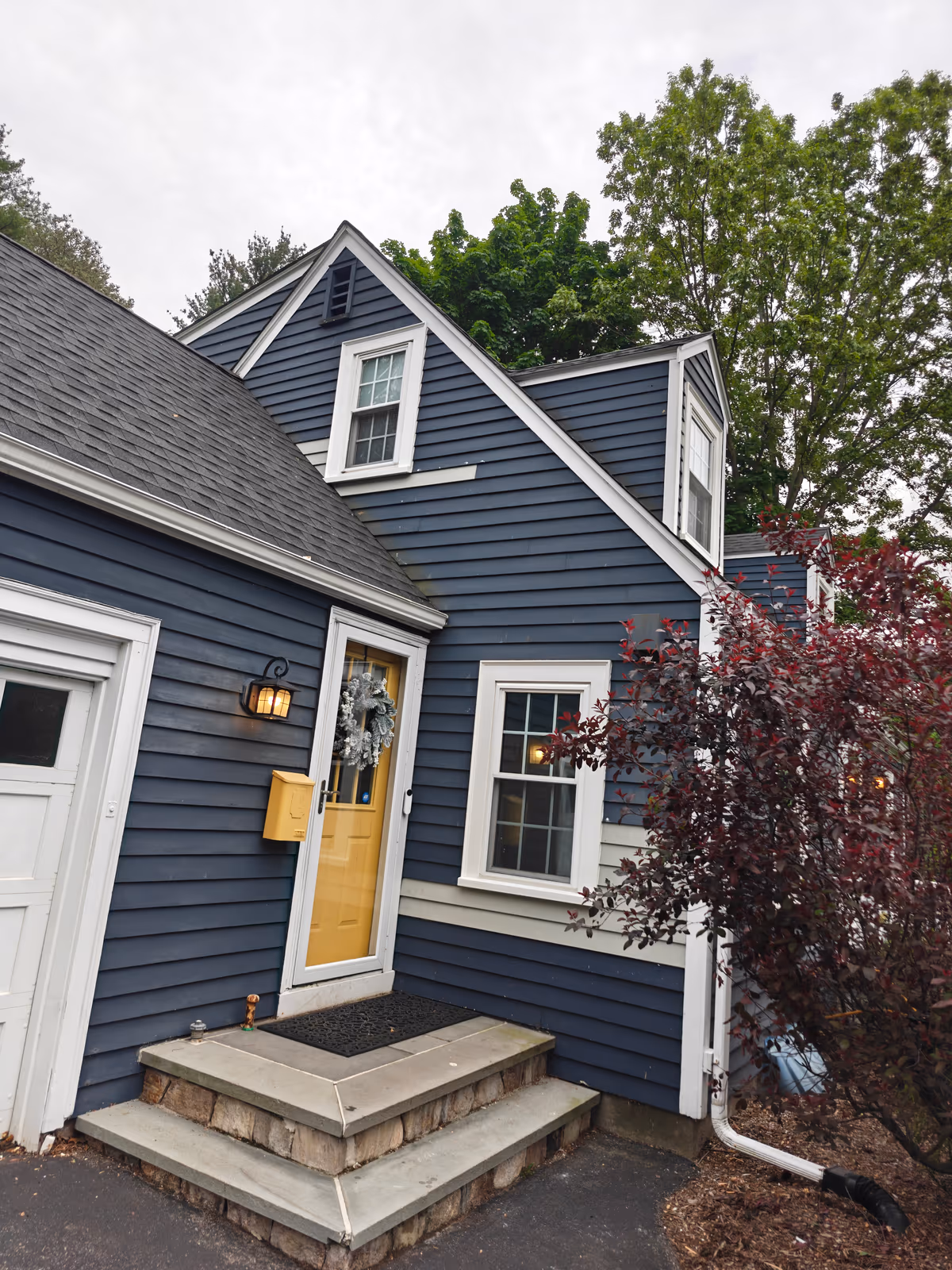 Blue-gray Cape Cod home with new white double-hung windows, a yellow front door and stone steps